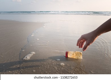 The Hand Of A Woman Is Picking Up A Plastic Bottle To Clean The Beach.