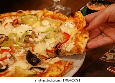 Hand Of A Woman Picking Up A Slice Of Vegetable Pizza.