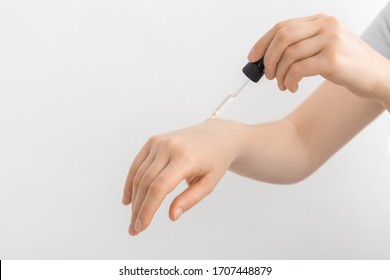 Hand Of Woman With Pipette Drop Of Serum Or Hyaluronic Acid On Gray Background. Hands Of A Beautiful Woman Dripping Serum Collagen.