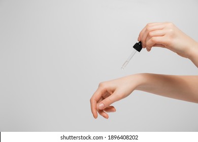 Hand Of Woman With Pipette Drop Of Serum Or Hyaluronic Acid On Gray Background. Hands Of A Beautiful Woman Dripping Serum Collagen.