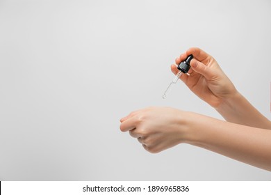 Hand Of Woman With Pipette Drop Of Serum Or Hyaluronic Acid On Gray Background. Hands Of A Beautiful Woman Dripping Serum Collagen.