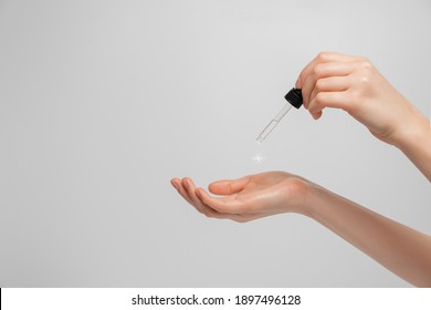 Hand Of Woman With Pipette Drop Of Serum Or Hyaluronic Acid On Gray Background. Hands Of A Beautiful Woman Dripping Serum Collagen.