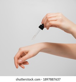 Hand Of Woman With Pipette Drop Of Serum Or Hyaluronic Acid On Gray Background. Hands Of A Beautiful Woman Dripping Serum Collagen.