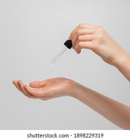 Hand Of Woman With Pipette Drop Of Serum Or Hyaluronic Acid On Gray Background. Hands Of A Beautiful Woman Dripping Serum Collagen.