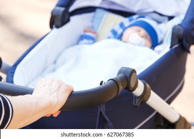 Hand Of Woman Pushing Babies Pram With Newborn Baby Sleeping Inside, Concept Of Child Care