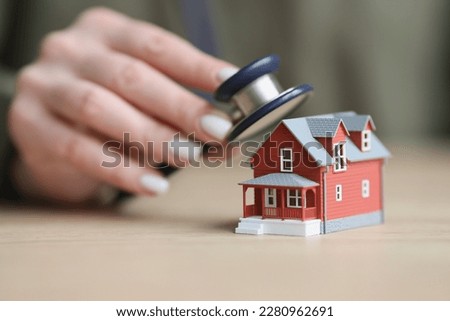 Hand of woman puts stethoscope to toy house standing on wooden table to check condition. Concept of diagnosis and care of item closeup