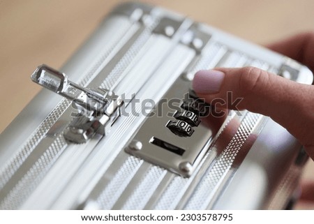 Hand of woman setting up password to unlock silver briefcase. Female person tries to opens bag with cash in office. Money safety and protection