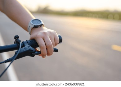 Hand of a woman using her fingers to hold brake while riding a bicycle on the country road at sunset, slow down the speed, spend more time for exercising or living concept