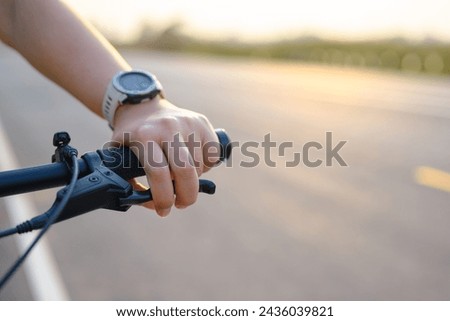 Hand of a woman using her fingers to hold brake while riding a bicycle on the country road at sunset, slow down the speed, spend more time for exercising or living concept