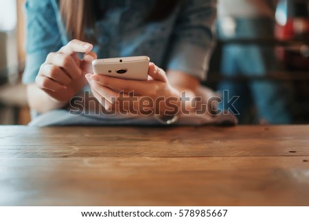 Hand of woman using smartphone on wooden table,Space for text or design.