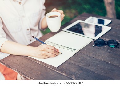 Hand woman writing notebook and holding cup coffee on wood table. - Powered by Shutterstock