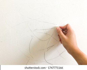 A Hand Woman(female) Using An Eraser Or Rubber.   Removing Pencil Stain On The White Wall In The Room.