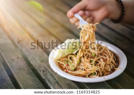 The hand of women scoop up the Spicy Green papaya salad called "Somtum" in Thai on wooden table with sunlight ray. Famous popular traditional yummy Thai food.