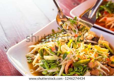 hand of women scoop up the Spicy papaya salad called "Somtum" in Thai on wooden table with sunlight ray. 