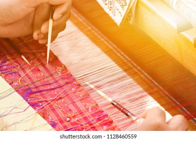 hand of a women works on silk weaving with traditional hand weaving loom.