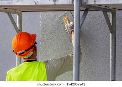 Hand Of Worker Applying Decorative Plaster On Wall By A Steel Trowel. White Cement Based Decorative Top Coat Plaster Resistant On Outside Whether Conditions. Selective Focus.