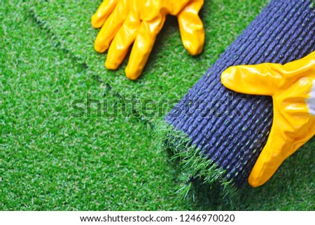 Hand of a worker in gloves with a artificial lawn grass. Artificial turf laying process. 