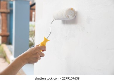 hand worker holding brush painting roller white on the wall house, diy and repair concept