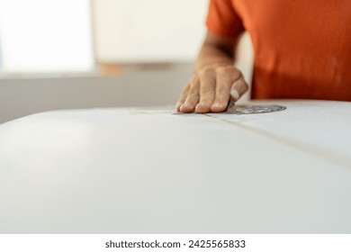 Hand of a worker sanding a surfboard in a repair shop - Powered by Shutterstock