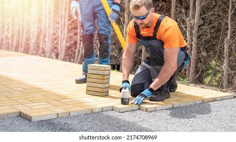 The hand of the worker using a rubber hammer for aligns the interlocking paving stone during the build of the sidewalk in thuja alley.