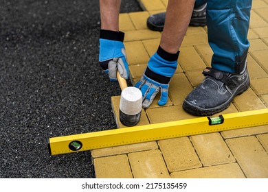 The hand of the worker using a rubber hammer and water-level for aligns the interlocking paving stone.