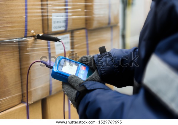 Hand of worker using\
thermometer to temperature measurement in the goods boxes with\
ready meals after import in the cold room or warehouse for keep\
temperature room