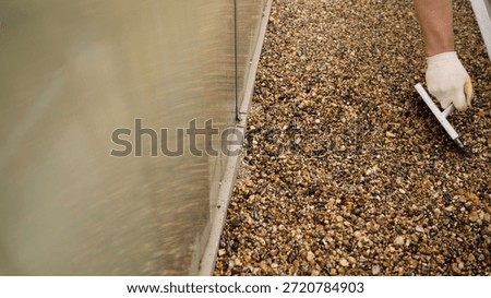Hand of a worker using a trowel to expertly smooth and finish a new resin bound gravel flooring surface during outdoor construction