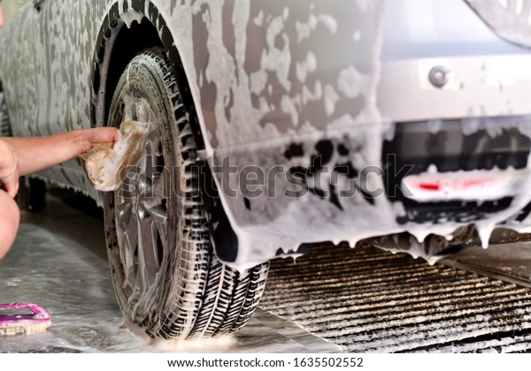  Hand a worker\
washing the top of a wheel disc, a fragment of the rear bumper of a\
car in soapy foam.