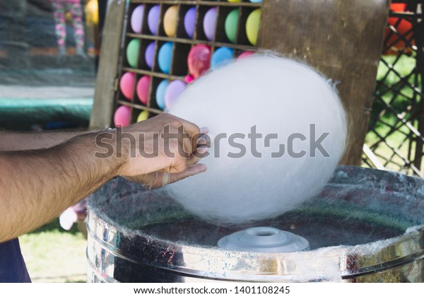 A hand wrap a cotton candy on a stick\
in a cotton candy machine. Making cotton\
candy