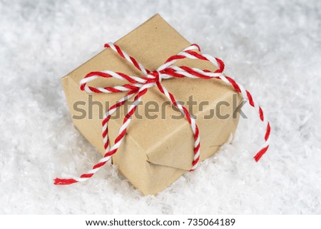 Hand wrapped plain paper small gift box tied with red and white twine, sitting on snow. Christmas, holiday giving or event sale concept.