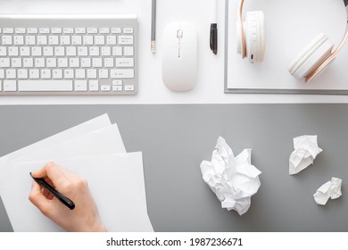 Hand writes notes piece paper in modern workspace  Crumpled pieces paper after writing working office desk and keyboard  headphones mouse office supplies  Home office workflow 