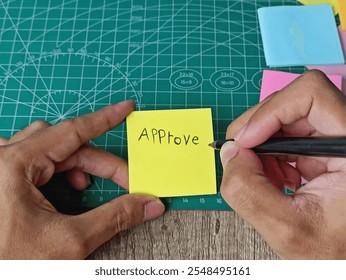 Hand Writing 'Approve' on Yellow Sticky Note with Pen on Cutting Mat. - Powered by Shutterstock