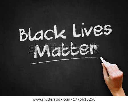 A hand writing 'Black Lives Matter' on chalk board for social issue concept design theme.