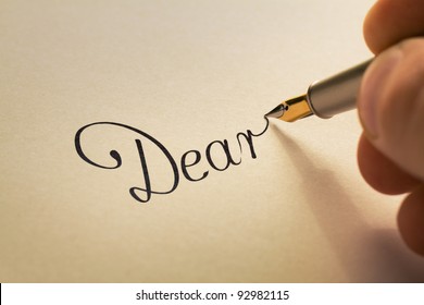hand is writing calligraphic letter starting with dear using old pen on yellow paper