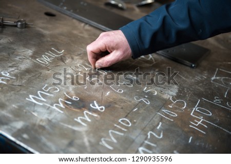 A hand writing with chalk notes on an industrial metal texture in an industrial workshop setting. chalk rustic metal marks.