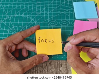 Hand Writing 'Focus' on Yellow Sticky Note with Pen on Cutting Mat. - Powered by Shutterstock