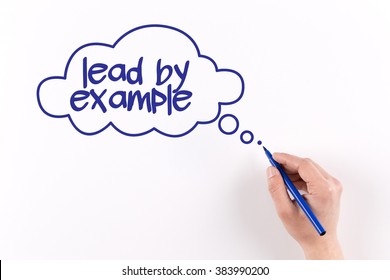 Hand writing LEAD BY EXAMPLE on white paper, view from above