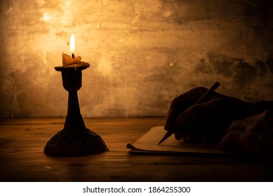 hand writing letter with pencil on paper in candle light condition