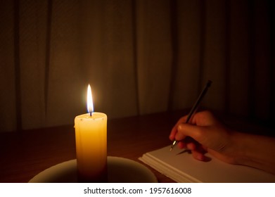 hand writing letter with pencil on paper in candle light condition. writing diary by candlelight in the dark.Relieve stress by writing in a calming environment.student writes in his notebook by dark
