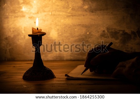 hand writing letter with pencil on paper in candle light condition