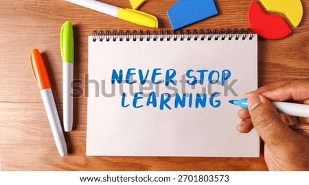 Hand writing Never Stop Learning on a notebook with colorful markers and geometric shapes on a wooden desk symbolizing education and growth.
