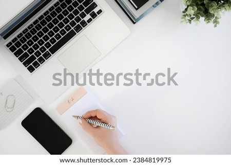 Hand writing notes next to a laptop computer on desk with props