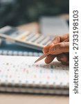 Hand writing notes in a notebook beside a calculator on office desk for budgeting and accounting. Personal finance planning, expense tracking, tax calculation, soft focus background, copy space.