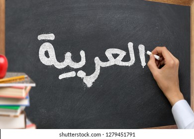 Hand writing on a blackboard in a 
Arabic language learning class course with the text "Arabic" written on it. with Some books and school materials concept.
