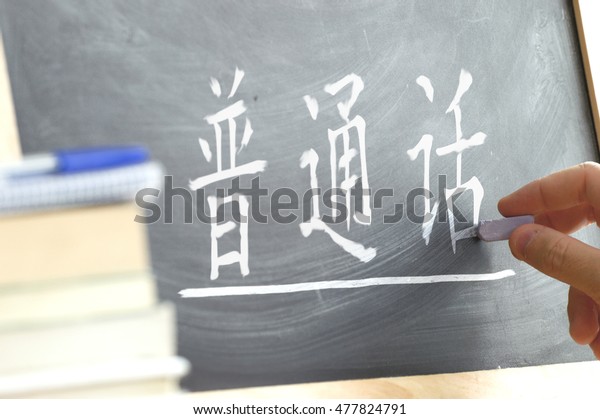 Hand writing on a blackboard in a language\
class with the word \