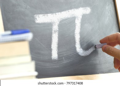 Hand Writing On A Blackboard In A Math Class With The PI Symbol Written On. Some Books And School Materials.