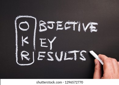 Hand Writing Text And Acronym Of OKR (Objective Key Results) On Chalkboard