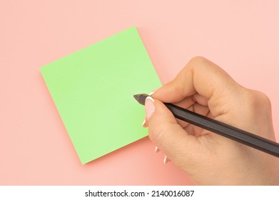 Hand written notes black pencil on green sticker. pink table background. woman hand writing on green sticky notes. Business people meeting and use notes to share idea on sticky note.
