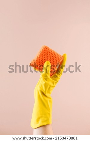 Hand in yellow glove holds sponge for dish washing on beige closeup copy space