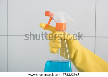 Hand in yellow glove holds sprayer with detergent. Housewife cleans house.